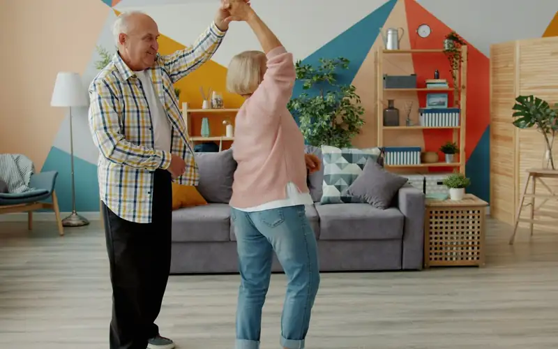 Ouder echtpaar danst samen in een lichte woonkamer