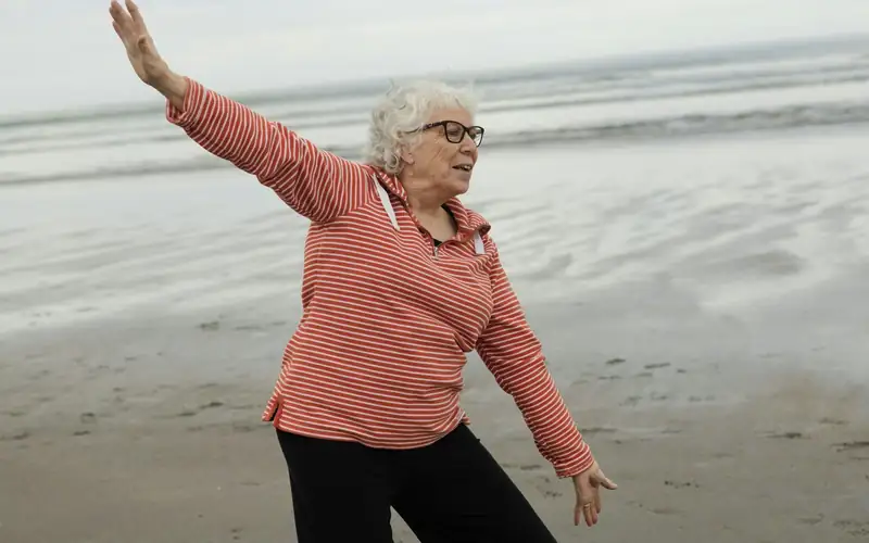 Oudere vrouw met grijs haar doet een tai-chi-oefening op het strand